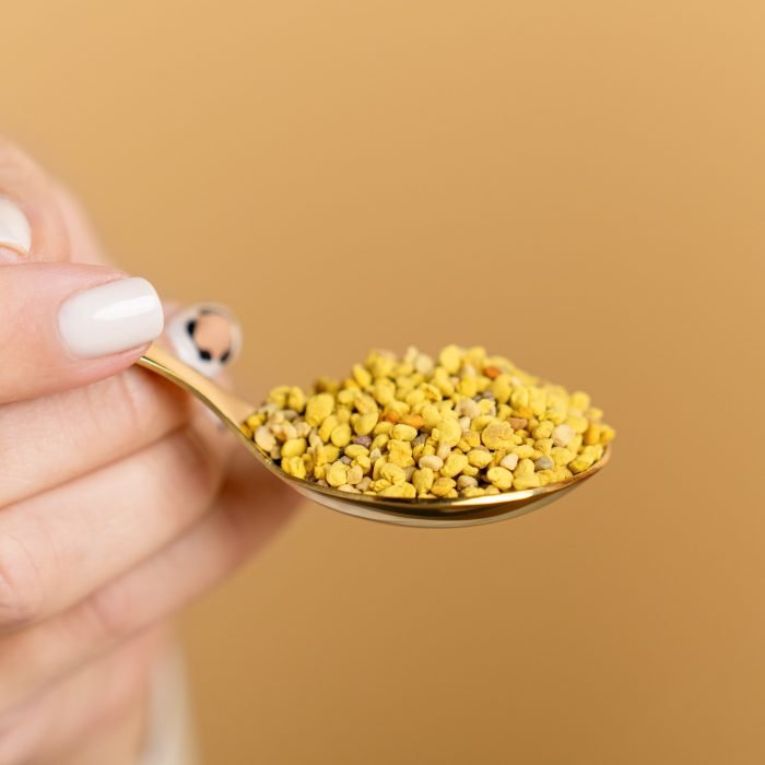 Nature’s Element – Bee Pollen Spoon Close-Up Hand holding golden spoon with Nature’s Element bee pollen – natural wellness supplement