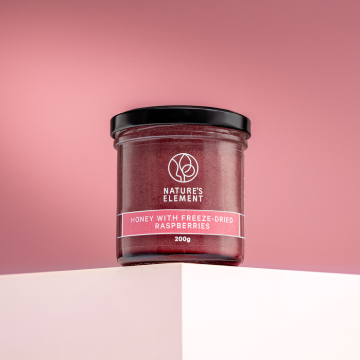 Nature’s Element honey with freeze-dried raspberries in glass jar on pink background – natural berry honey
