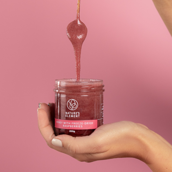 Person holding open jar of Nature’s Element raspberry honey with dipper – natural fruit honey
