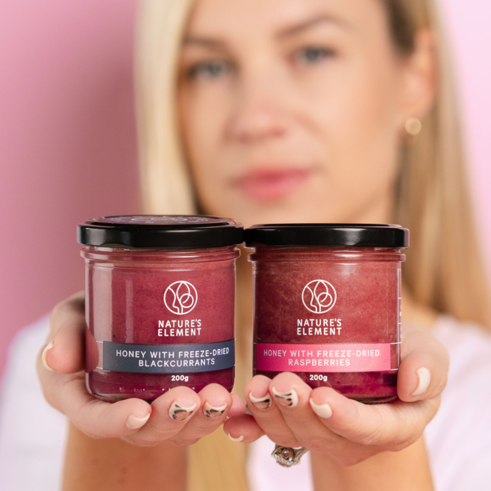Person holding jars of Nature’s Element honey with raspberries and blackcurrants – natural berry honey collection
