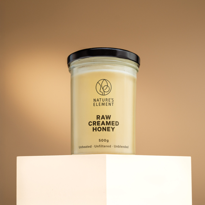 Nature’s Element raw creamed honey in glass jar on warm beige background – unheated natural honey