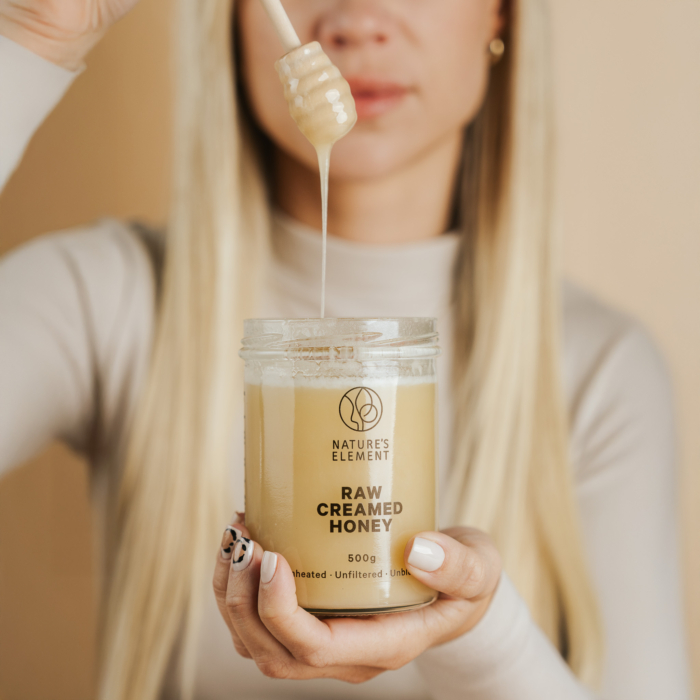 Person holding jar of Nature’s Element raw creamed honey with dipper – natural Irish honey