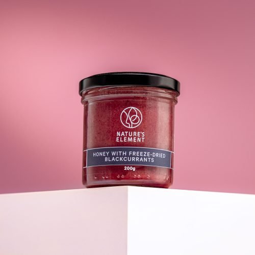 Nature’s Element – Honey with Freeze-Dried Blackcurrants 200g Nature’s Element honey with freeze-dried blackcurrants in glass jar on pink background – natural berry honey