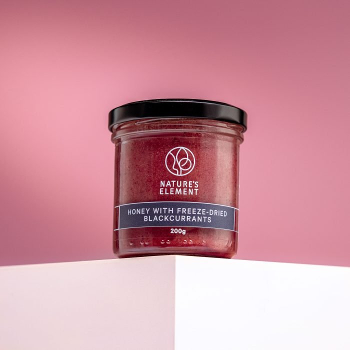 Nature’s Element – Honey with Freeze-Dried Blackcurrants 200g Nature’s Element honey with freeze-dried blackcurrants in glass jar on pink background – natural berry honey
