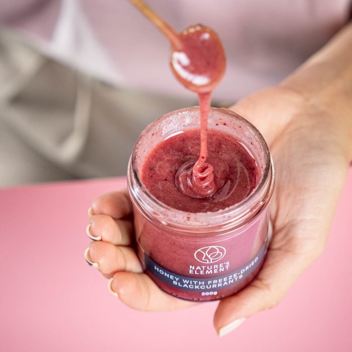 Nature’s Element – Blackcurrant Honey Lifestyle Person holding open jar of Nature’s Element blackcurrant honey with dipper – natural fruit honey