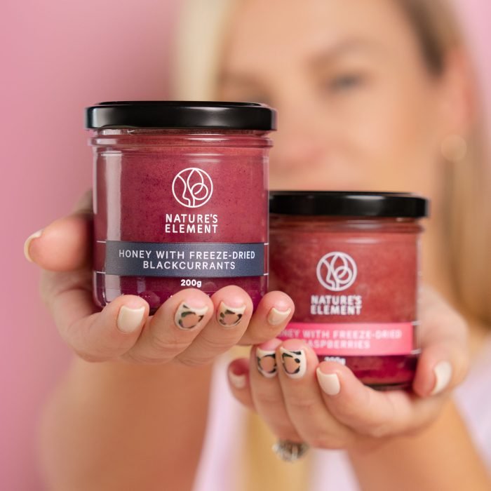 Nature’s Element – Blackcurrant & Raspberry Honey Jars Person holding Nature’s Element blackcurrant and raspberry honey jars – natural fruit-infused honey collection