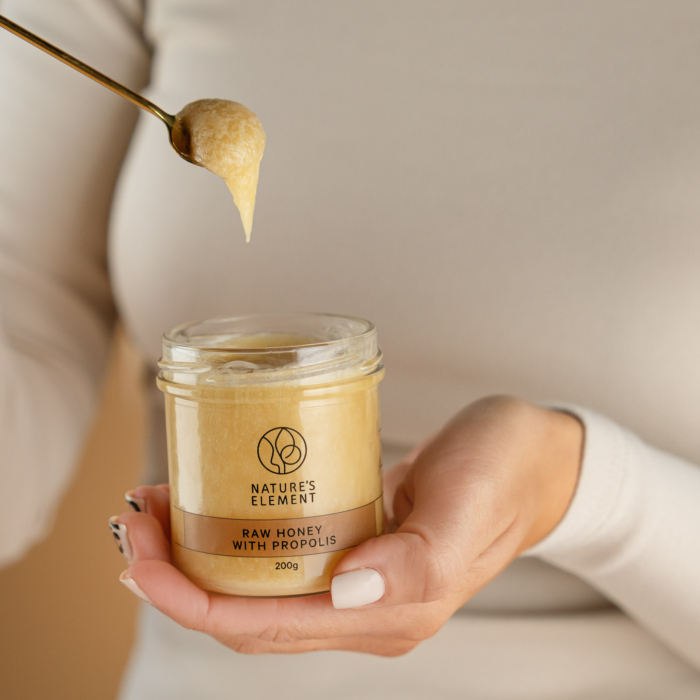 Person holding spoonful of Nature’s Element honey with propolis – natural wellness blend