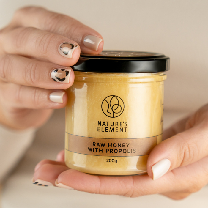 Person holding jar of Nature’s Element raw honey with propolis – natural immune health product