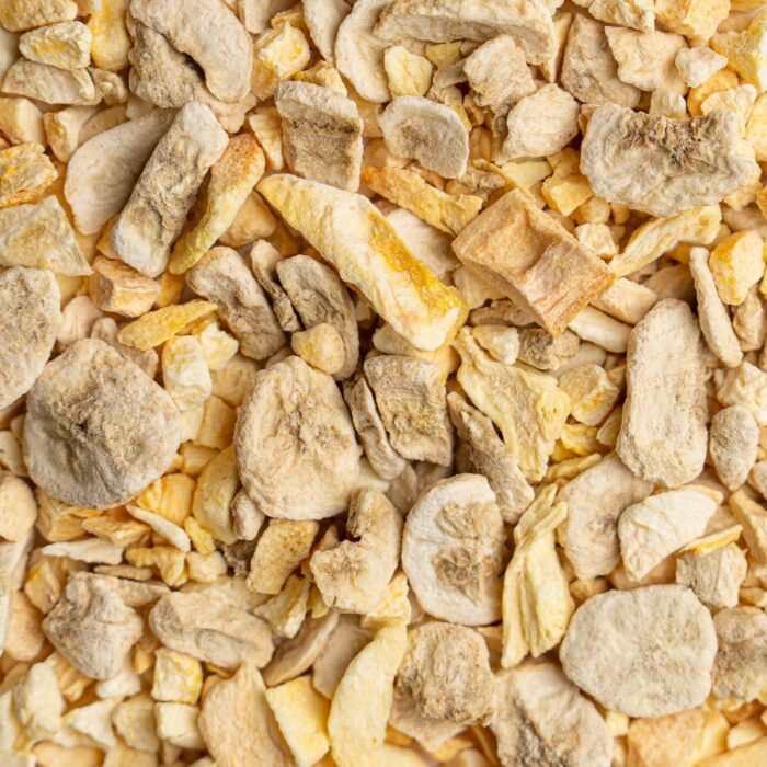 Overhead view of mixed freeze-dried tropical fruits showing banana slices, mango chunks, pineapple pieces and peach with natural texture