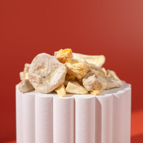Freeze-dried tropical fruit mix showing banana slices, mango chunks, pineapple pieces and peach slices on white pedestal